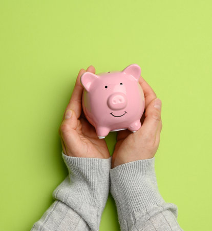 hand holding pink ceramic piggy bank on a green background, close upの写真素材