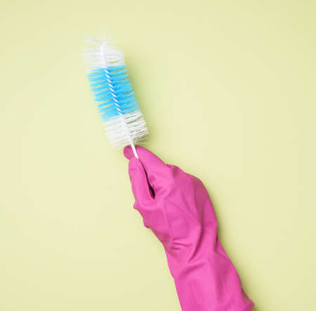 hand in a rubber glove holds a brush for washing bottles on a green background, close upの写真素材