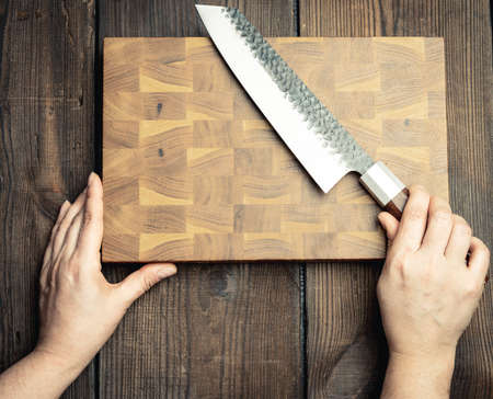 metal kitchen knife and wooden cutting board on a table made of brown wooden boards, top view