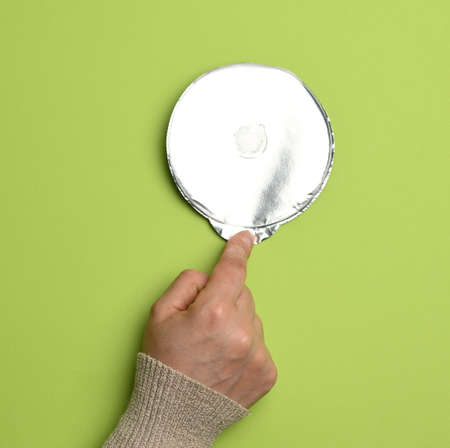 round aluminum thin lid for plastic yogurt jars on a green background, close up