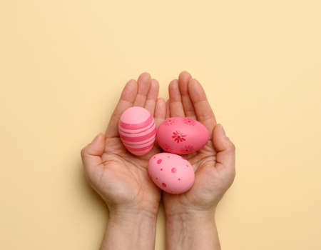 female hand holding multicolored decorative easter eggs on a beige background, top viewの写真素材