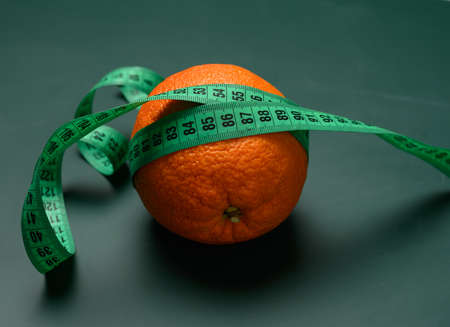 orange wrapped in green measuring tape, slimming concept, cellulite, close upの写真素材