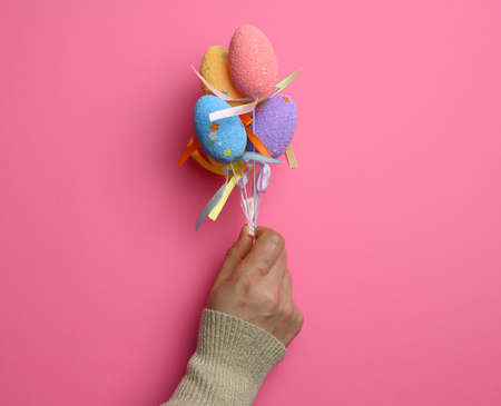 female hand holding multicolored decorative easter eggs on pink background, close up