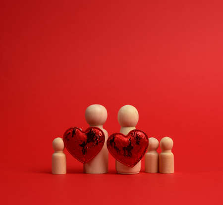 pair of wooden men of the bride and groom, between them a red heart, red background, the concept of love and relationshipsの写真素材