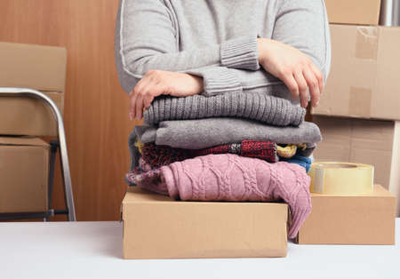 woman in a gray sweater is packing clothes in a box, the concept of assistance and volunteering,...