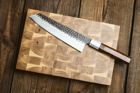 metal kitchen knife and wooden cutting board on a table made of brown wooden boards, top view