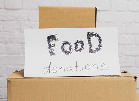 stack of cardboard boxes and white sheet of paper with inscription food donation on white brick wall backgroundの写真素材