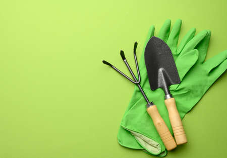 green rubber gloves and garden set of shovels, rakes, pitchforks on a green background, top view, flat layの写真素材