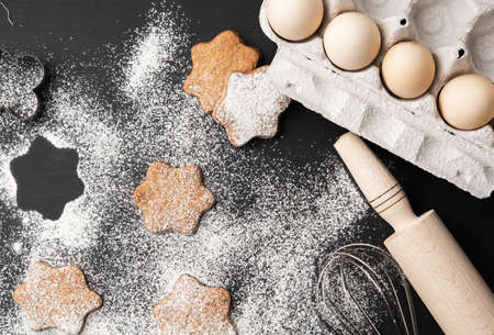 baked star-shaped gingerbread cookie sprinkled with powdered sugar on a black table and ingredients, top viewの写真素材