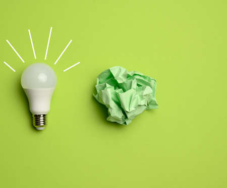 crumpled colored balls of paper and glass white lamp on green background, top viewの写真素材
