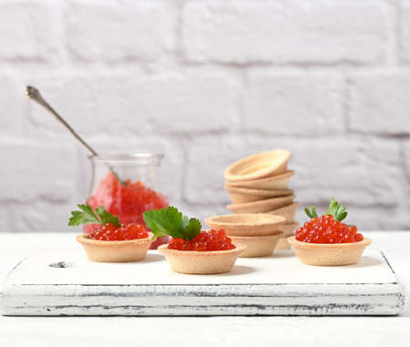 red caviar in a glass jar and round tartlets on a white table, close upの写真素材