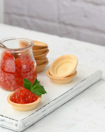 red caviar in a glass jar and round tartlets on a white table, close upの写真素材