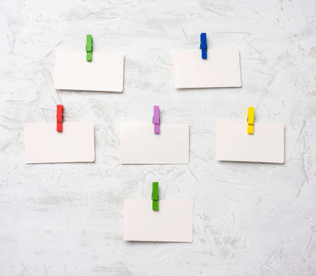 blank white cardboard rectangular pieces of paper hanging on clothespins, white cement wall backgroundの写真素材