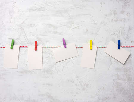 blank white cardboard rectangular pieces of paper hanging on clothespins, white cement wall backgroundの写真素材
