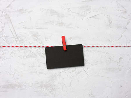 blank black cardboard rectangular sheet of paper hang on clothespins, white cement wall backgroundの写真素材