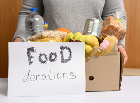 woman in a gray sweater is packing food in a cardboard box, the concept of assistance and volunteering, donationの写真素材