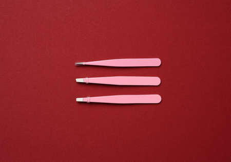 various metal eyebrow tweezers on a red background, top viewの写真素材