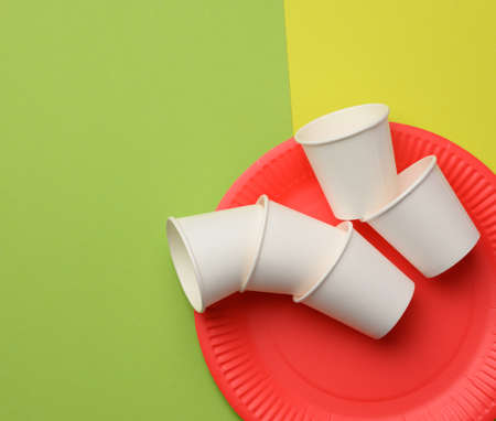 stack of white paper cups and red round plates on a green background. Plastic rejection concept, zero wasteの写真素材