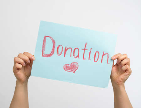 female hand holding a blue piece of paper with the inscription donation on a white backgroundの写真素材