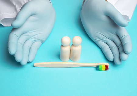 wooden figurines and hands of a doctor in medical blue gloves, next to a wooden toothbrushの写真素材