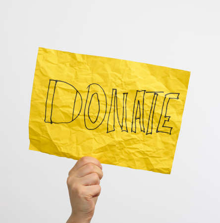 female hand holds a yellow sheet of paper with the inscription donate, close upの写真素材