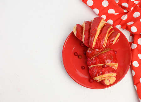 two baked croissants with cherry glaze on a red ceramic plate, white table, top viewの写真素材