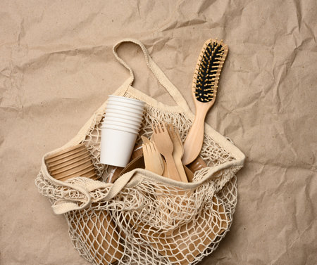 white string bag with disposable paper dishes and wooden forks on brown kraft paper, top view, zero wasteの写真素材