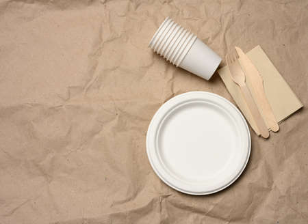 disposable round white paper plates and cups on brown paper background, top view, zero wasteの写真素材