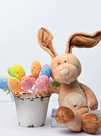 teddy bunny sitting on a white background and decorative colorful easter eggs, close upの写真素材