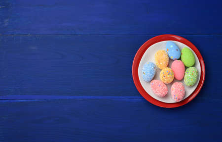 decorative easter eggs in a round white ceramic plate on a blue wooden plank background, top viewの写真素材