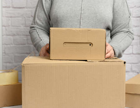 woman in a gray sweater holding a brown cardboard box, moving, donation