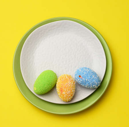 decorative easter eggs in a round white ceramic plate on a yellow background, top view