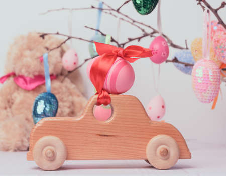 wooden toy car carrying a pink Easter egg fixed with a red ribbon, white background, close upの写真素材