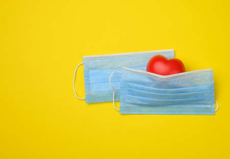red heart lies on a white disposable medical mask, yellow background, copy spaceの写真素材