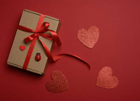 rectangular brown cardboard box tied with a silk red ribbon on a red background, top view, close up
