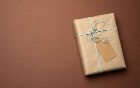 box wrapped in brown kraft paper and tied with rope, gift on a brown background, top view