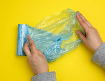 female hand unwinds a blue plastic bag for rubbish, yellow background, top viewの写真素材