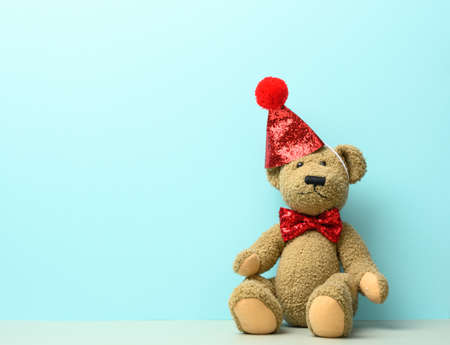 brown teddy bear in a red cap sits on a blue background, place for inscriptionの写真素材