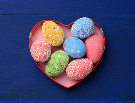 decorative easter eggs in a cardboard box on a blue wooden background, top view