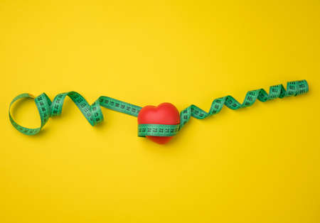 red heart and green measuring tape on yellow background, top viewの写真素材