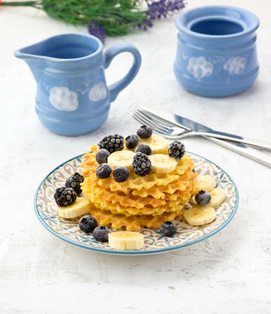 stack of baked Belgian waffles on a round plate with berries on a white table, delicious breakfast, close upの写真素材