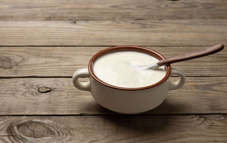 sour cream in a brown ceramic bowl with a wooden spoon on a table, fermented milk useful product, top viewの写真素材
