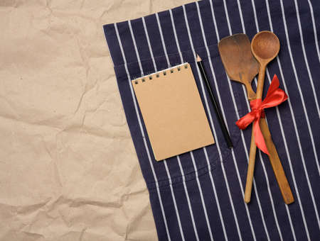 blue chef's apron, wooden spoons and notebook with blank brown sheets, top viewの写真素材