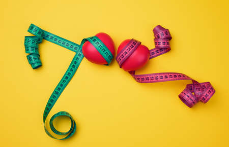 red heart and green measuring tape on yellow background, top viewの写真素材