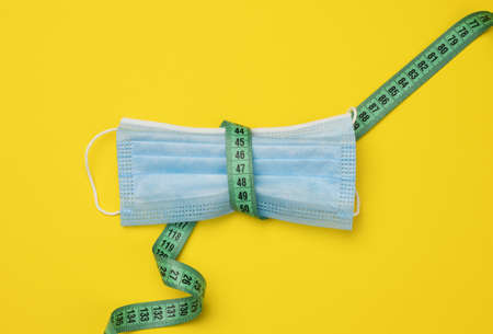 blue disposable medical mask on a yellowe background, personal protective equipment for the...