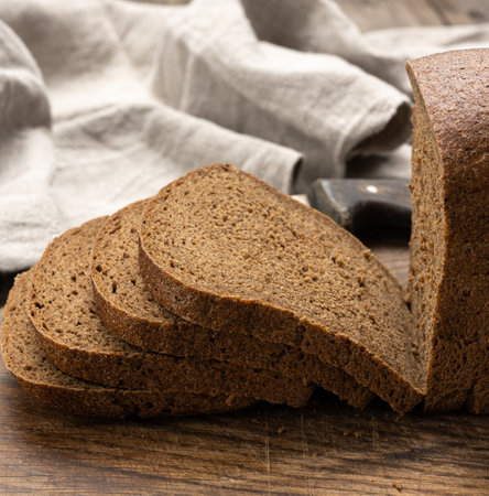 sliced baked rectangular rye flour bread on brown board, healthy food, close up