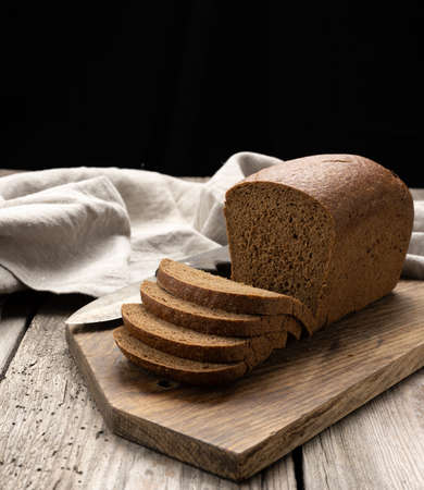 sliced baked rectangular rye flour bread on brown board, healthy food, close up