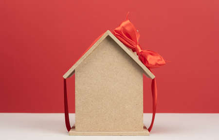 model of a wooden house tied with a red silk ribbon on a red background, concept of real estate purchase, mortgageの写真素材