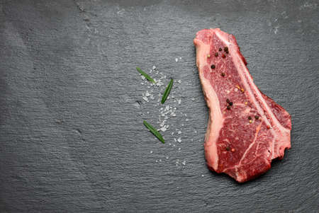 fresh raw piece of beef meat, striploin steak lies on a black board with spices, top viewの写真素材