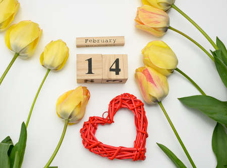 yellow tulips, wooden calendar with date 14 February and red heart on white background, top view